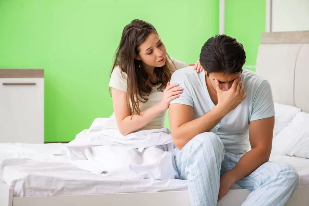 Woman comforting upset man in bed