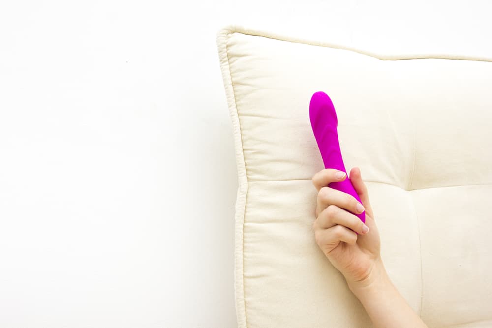 woman holding pink dildo in bed